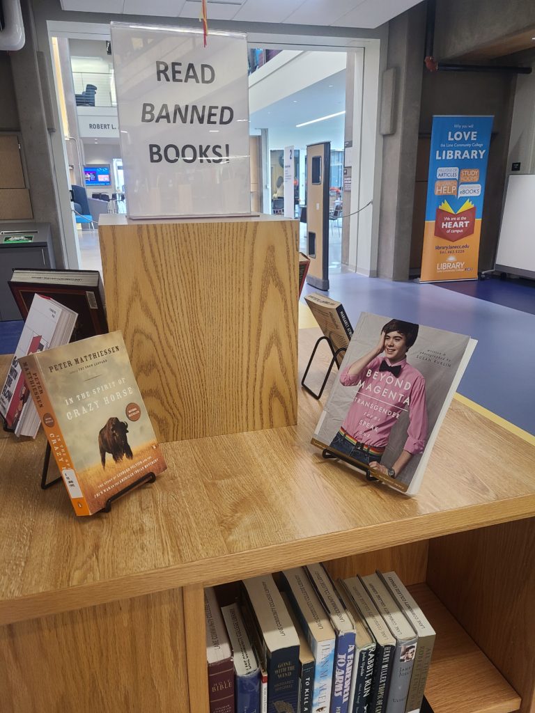A white sign reads "Read banned books". Two books sit underneath, one titled Beyond Magenta and the other is called In The Spirit of Crazy Horse
